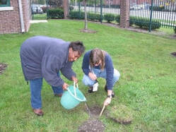 Two City of Toledo staff members pour water into a shallow hole dug into a yard to perform a percolation test.